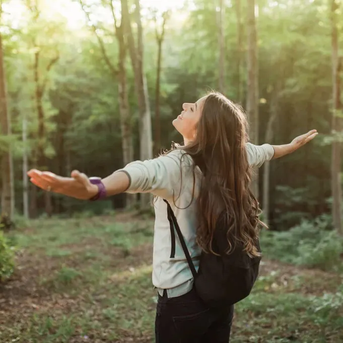 Woman in a sunlit forest, arms spread wide